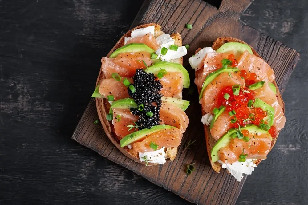 Lachs mit Kaviar und Lachsroggen auf Brot mit Crème fraîche und Avocado
