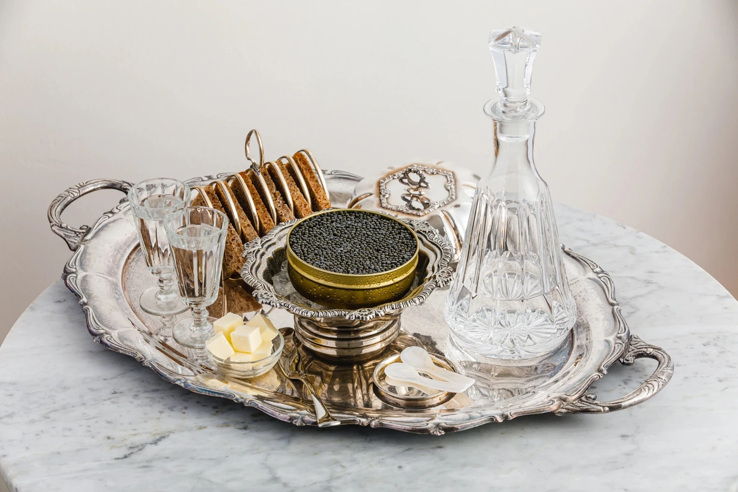 Kaviar in Kaviardose auf Kaviarschale, mit Wodka in Gläsern, dunklem Brot, Butter, Perlmuttlöffel und Karaffe mit Wodka
